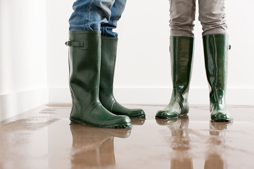 People in boots stand in a puddle. Why Is My Furnace Leaking Water?