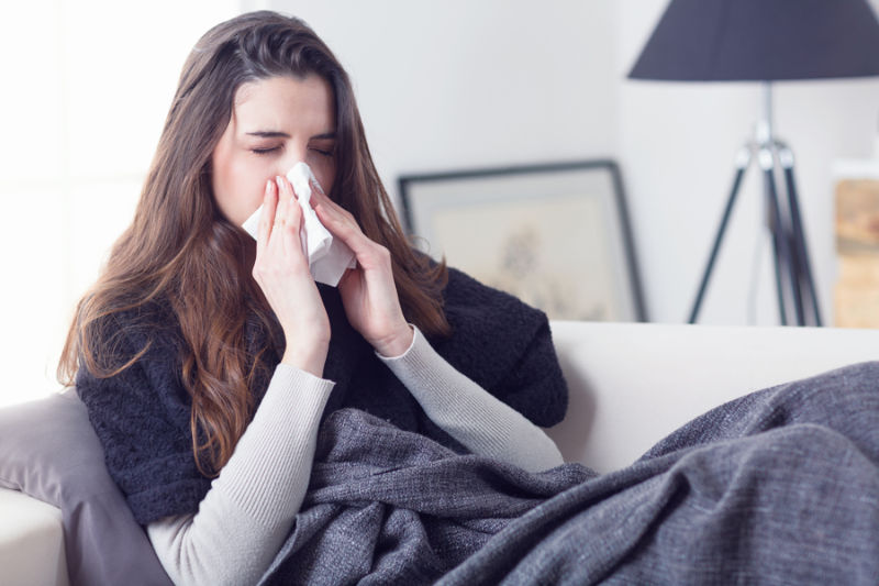 Woman sneezing nose with tissue.