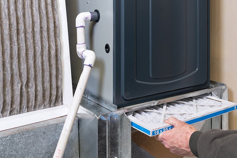A person replacing the air filter in an HVAC furnace system.