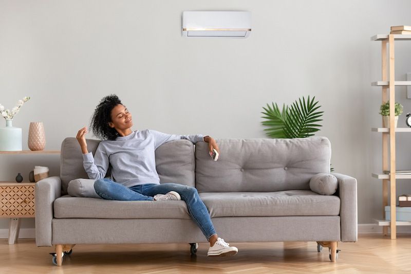 What Indoor Air Quality Accessories Can Help Keep Me Healthy? Image shows woman sitting on grey couch and looking relaxed.